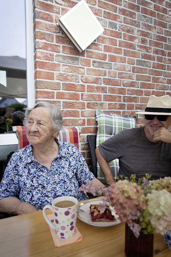 Eine ältere Dame sitzt auf der Terrasse, vor ihr ein Stück Kuchen und Kaffee